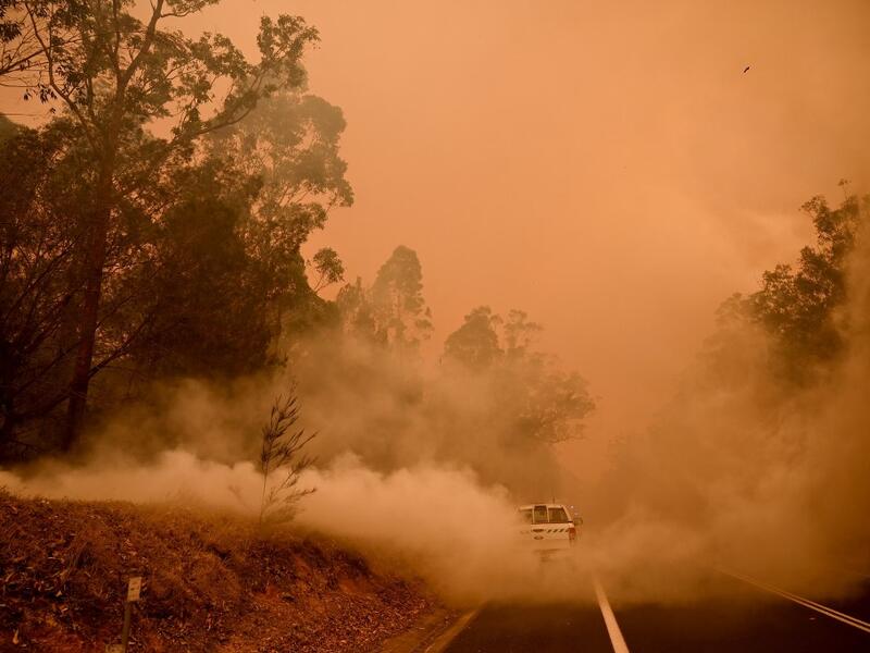 Firefighters tackle a bushfire in thick smoke in the town of Moruya, south of Batemans Bay, in New South Wales on January 4, 2020. Up to 3,000 military reservists were called up to tackle Australia's relentless bushfire crisis on January 4, as tens of thousands of residents fled their homes amid catastrophic conditions. PETER PARKS / AFP