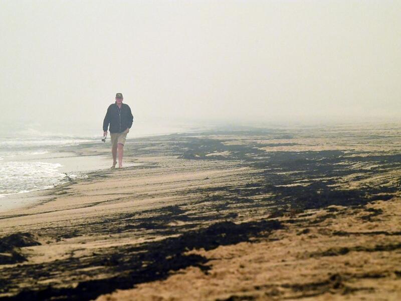 Local resident Dave Iredale walks past ash from bushfires washed up on a beach in Merimbula, in Australia's New South Wales state on January 5, 2020. Australians on January 5 counted the cost from a day of catastrophic bushfires that caused "extensive damage" across swathes of the country and took the death toll from the long-running crisis to 24. SAEED KHAN / AFP