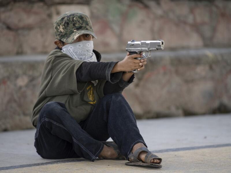 A boy aims a gun as the Regional Coordinator of Community Authorities (CRAC-PF) community police force teaches a group of children how to use weapons, at a basketball court in the village of Ayahualtempan, Guerrero State, Mexico, on January 24, 2020. The CRAC-PF vigilante group trains children as young as five so they can protect themselves from drug-related criminal groups operating in the area. Pedro PARDO / AFP