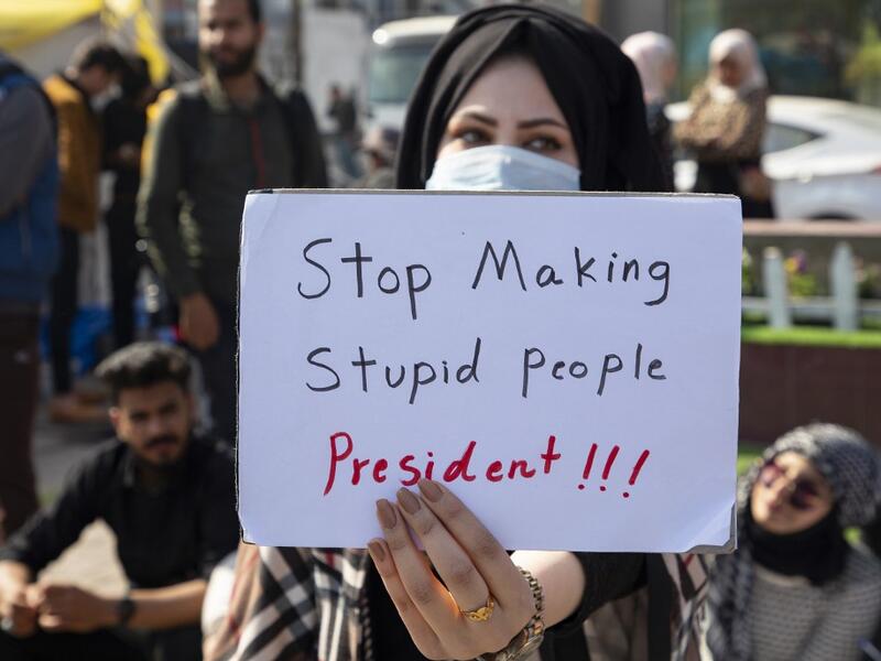 An Iraqi anti-government protester wearing a protective mask lifts a placard during a student demonstration in the southern city of Basra, on February 6, 2020, after a night of violence blamed on supporters of a powerful cleric. AFP