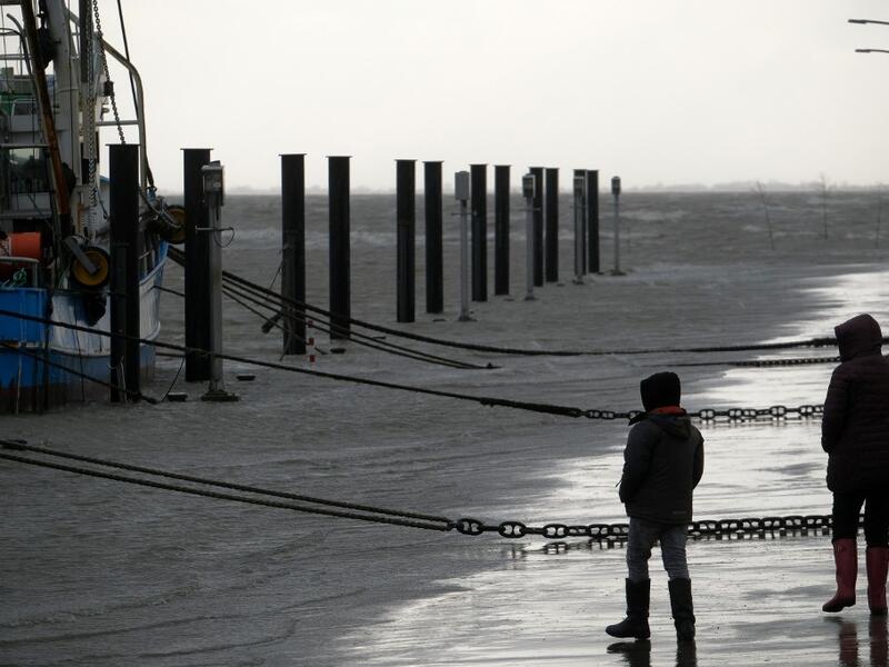 People walk near fish trawlers at the flooded harbor of Wremen, on the North Sea near Bremerhaven, northern Germany, on Febuary 11, 2020. Fierce winds and heavy rains claimed at least six lives across northern Europe on February 11, 2020, as Storm Ciara disrupted travel, grounded hundreds of flights, flooded roads and left vast areas without power. Patrik Stollarz / AFP