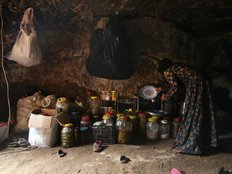 A woman holds a plate and a saucepan as she stands by food stores including pickled olives inside an underground shelter where several families of internally displaced Syrians from Aleppo and Idlib provinces are taking refuge, in the village of Taltunah about 15 kilometres northwest of Idlib in the northwestern Idlib province, on February 23, 2020. Aref TAMMAWI / AFP