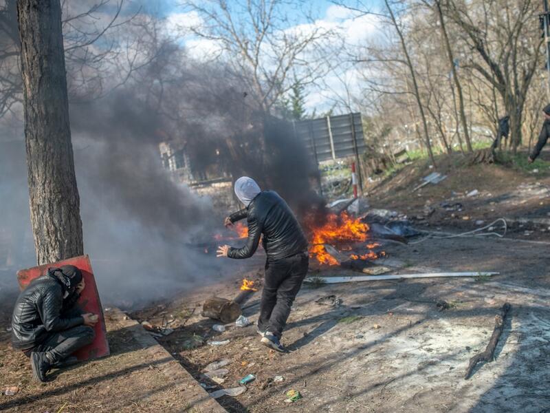 A man throws a stone to Greek police as another takes cover behind a tree during clashes in the buffer zone at Turkey-Greece border, at Pazarkule, in Edirne district, on February 29, 2020. Thousands of migrants stuck on the Turkey-Greece border clashed with Greek police on February 29, 2020, according to an AFP photographer at the scene. BULENT KILIC / AFP