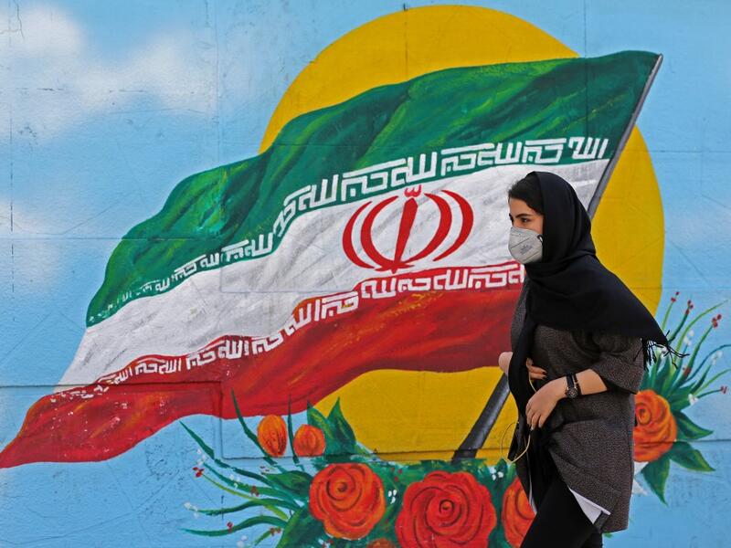 Iranians wearing masks walk past a mural displaying their national flag in Tehran on March 4, 2020. Iran has scrambled to halt the rapid spread of the COVID-19 virus, shutting schools and universities, suspending major cultural and sporting events, and cutting back on work hours.  ATTA KENARE / AFP