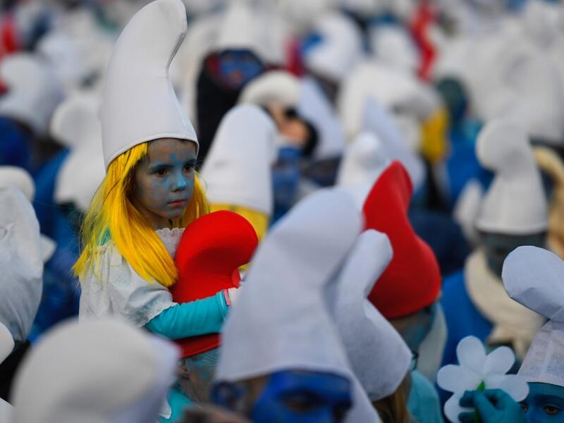A child dressed as Smurfs ('Schtroumpfs' in French), a Belgian comic franchise centered on a fictional colony of small, blue, human-like creatures who live in mushroom-shaped houses in the forest, sits on the shoulders of an adult during a world record gathering of Smurfs on March 7, 2020, in Landerneau, western France. Damien MEYER / AFP