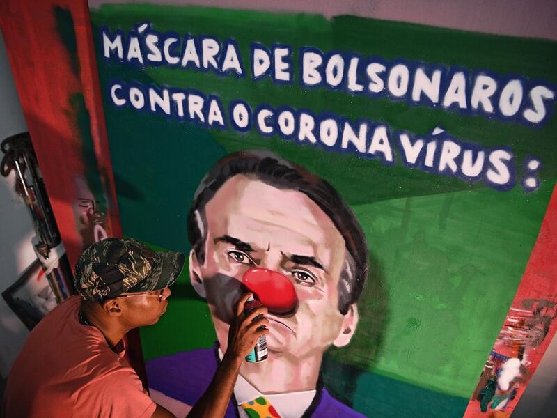 Brazilian graffiti artist Aira Ocrespo finishes an art piece featuring Brazil's President Jair Bolsonaro reading "Bolsonaro's mask against the Coronavirus" at his studio in Rio de Janeiro, Brazil, on March 18, 2020. Bolsonaro gave a press conference today wearing a facemask as he spoke about the COVID-19 coronavirus pandemic. CARL DE SOUZA / AFP
