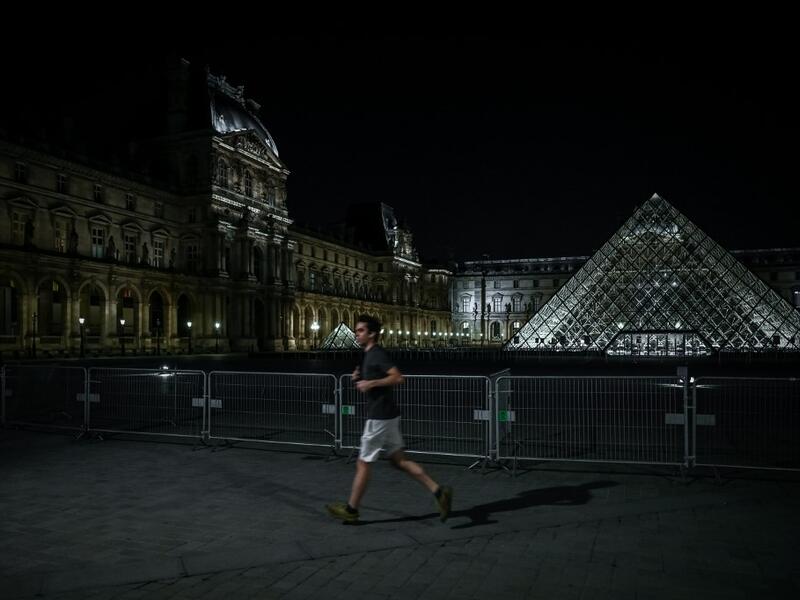 A man jogs past the Louvre Pyramid at night in Paris on March 18, 2020, as a strict lockdown came into in effect in France to stop the spread of COVID-19, caused by the novel coronavirus. A strict lockdown requiring most people in France to remain at home came into effect at midday on March 17, 2020, prohibiting all but essential outings in a bid to curb the coronavirus spread. The government has said tens of thousands of police will be patrolling streets and issuing fines of 135 euros ($150) for people wit