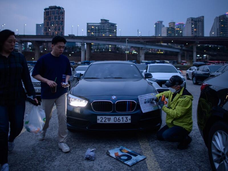 In a photo taken on March 21, 2020 a staff member secures newspaper over the headlights of cars prior to a screening at a drive-through cinema in Seoul. Box office numbers in South Korea -- which has 8,897 confirmed virus cases -- have plummeted in recent weeks due to the epidemic, with authorities urging the public to avoid large crowds. But at drive-in cinemas, moviegoers can enjoy a movie from the comfort of their cars, parked in front of a large outdoor screen.  Ed JONES / AFP