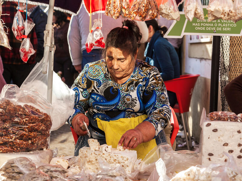 Elderly woman chops blocks of nougat at a market in Portugal (Shutterstock) 