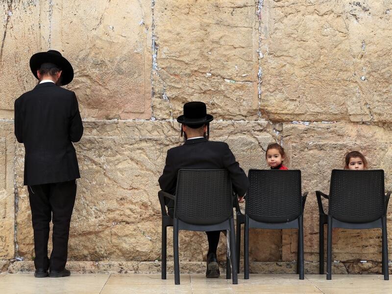 Children sit in chairs next to ultra-Orthodox Jewish men praying at the nearly deserted Western Wall, the holiest site where Jews can pray, after Israel has imposed some of the world's tightest restrictions to contain COVID-19 coronavirus disease, in Jerusalem on March 12, 2020. Israel imposed a two-week quarantine on all travellers entering the country, almost stopping tourism and limiting public gatherings as officials confirmed its 100th case of the COVID-19 coronavirus disease. Emmanuel DUNAND / AFP