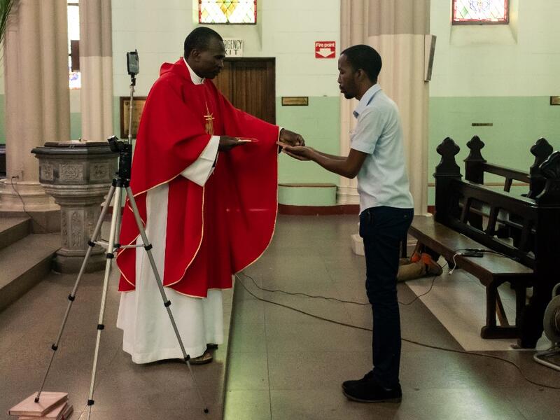 Father Kennedy Mugute, the Vicar General of the Archdiocese of Harare, gives communion to the head of media Ronald Mapfumo (R), as he conducts a Palm Sunday mass, which is livestreamed to parishioners on Facebook, in the empty Cathedral of the Sacred Heart in Harare, on April 5, 2020, on the seventh day of a lockdown in Zimbabwe. AFP