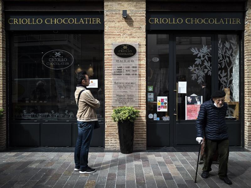 A client leaves Criollo chocolate maker shop after buying Easter chocolates as another one waits outside to respect the rules of social distancing in shops on April 7, 2020 in Toulouse, southern France, on the twenty-second day of a strict lockdown in France to stop the spread of COVID-19, caused by the novel coronavirus. Lionel BONAVENTURE / AFP