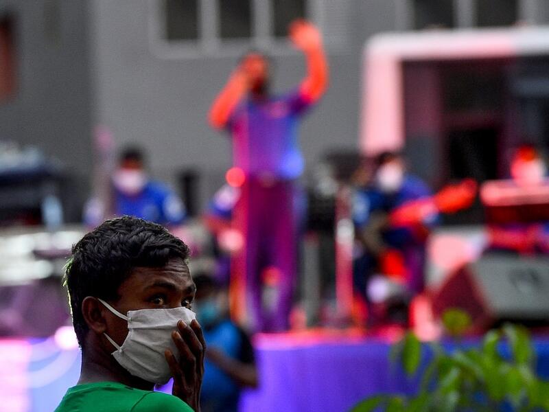 A resident wearing a facemask watches a music band formed by Sri Lankan Navy personnel as they play outside a housing complex during a government-imposed nationwide lockdown as a preventive measure against the COVID-19 coronavirus, in Colombo on April 9, 2020. ISHARA S. KODIKARA / AFP