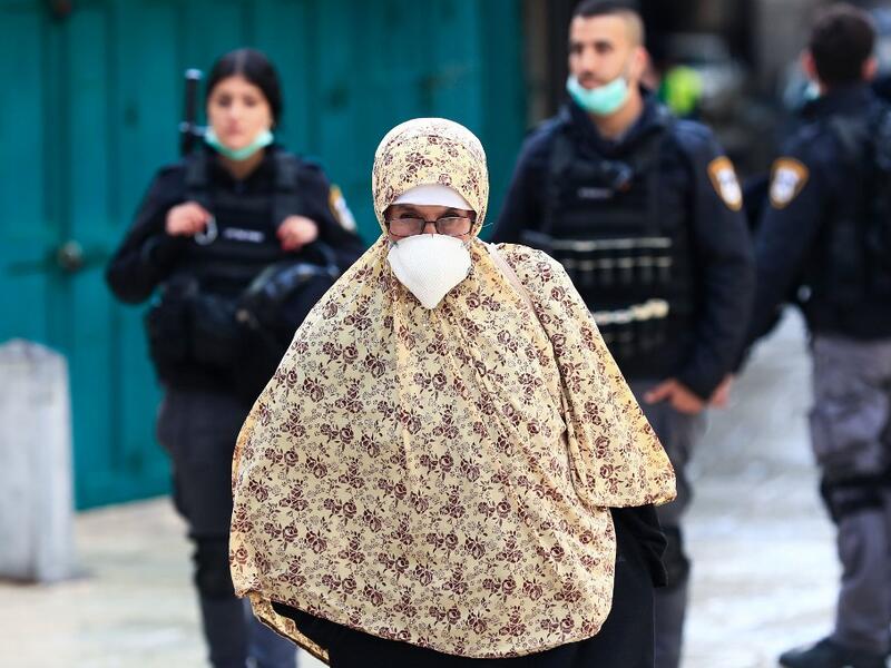 A woman wearing a protective mask amid the COVID-19 outbreak, makes her way along the Via Dolorosa while Israeli policemen patrol the mostly empty route, during Good Friday in Jerusalem, on April 10, 2020. All cultural sites in the Holy Land are shuttered, regardless of their religious affiliation, as authorities seek to forestall the spread of the deadly respiratory disease, which will prevent Christians from congregating for the Easter service, this coming Sunday for Catholic worshippers, then a week late