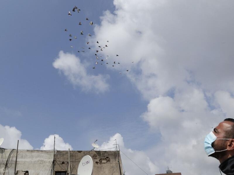 A pigeon owner, wearing personal protective equipment, watches his pigeons fly on the rooftop of his building in the southern suburb of Beirut on April 11, 2020. ANWAR AMRO / AFP