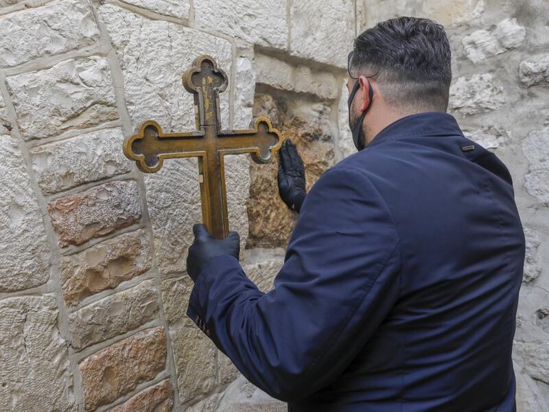 A Christian worshipper wearing a face mask, due to the COVID-19 coronavirus pandemic, touches one of the stations of the Via Dolorosa (Way of Sorrow), the path traditionally believed to have been taken by Christ while on the way to be crucified, to receive a blessing, in the old city of Jerusalem on Orthodox Holy Friday April 17, 2020. AHMAD GHARABLI / AFP