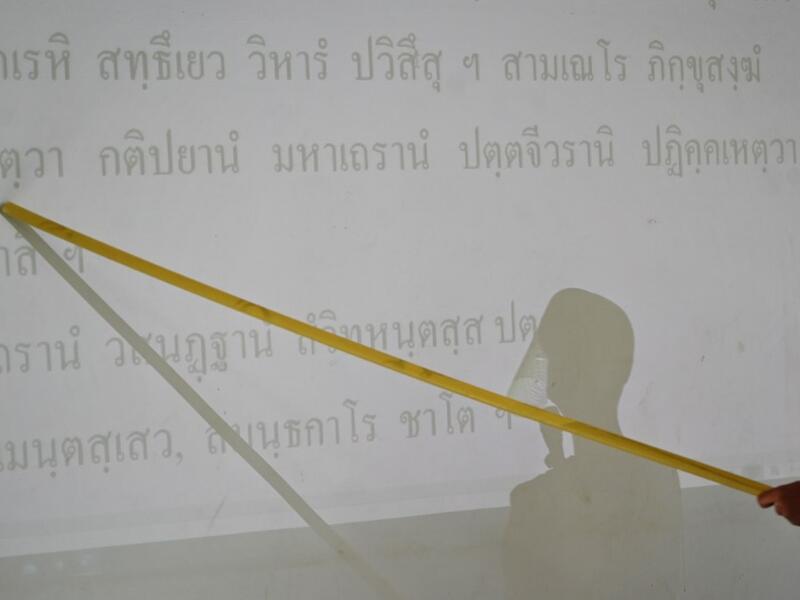 A novice monks wearing a face shield as a preventive measure against the spread of the COVID-19 coronavirus reads religious text off a projection during religious studies at Wat Molilokkayaram Buddhist temple in Bangkok on April 20, 2020. Lillian SUWANRUMPHA / AFP