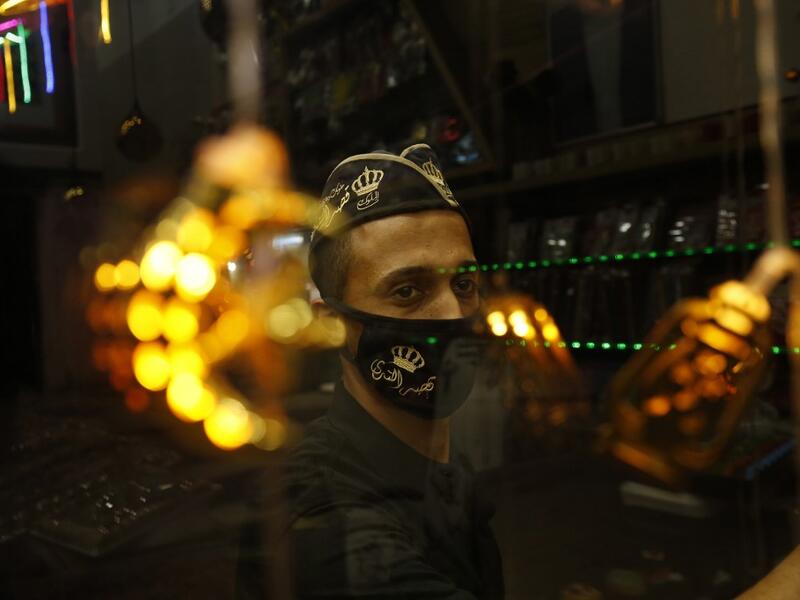 A Palestinian worker at a desserts shop wipes the surface of its window while clad in a face mask, a precaution due to the COVID-19 coronavirus pandemic, in Rafah in the southern Gaza Strip on the second night of the Muslim holy month of Ramadan early on April 25, 2020, as people shop for supplies at the start of the holy month. SAID KHATIB / AFP