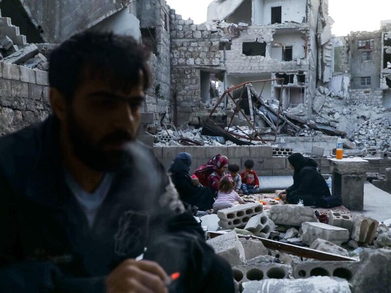 This picture taken on May 4, 2020 during the Muslim holy fasting month of Ramadan shows Tareq Abu Ziad (L), a displaced Syrian from the town of Ariha in the southern countryside of the Idlib province, smoking as members of his family break their fast together for the sunset "iftar" meal, in the midst of the rubble of their destroyed home upon their return to the town for one day after fleeing during the previous military assault by Syrian government forces and their allies. AAREF WATAD / AFP
