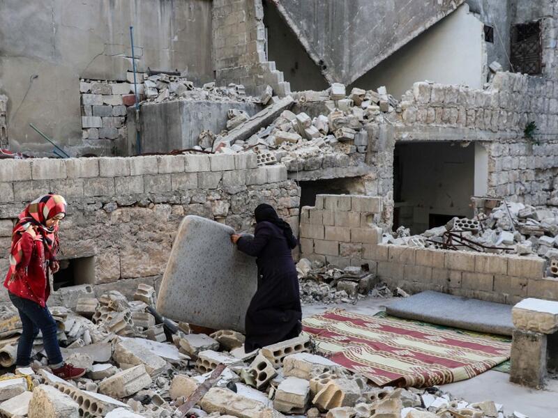 This picture taken on May 4, 2020 during the Muslim holy fasting month of Ramadan shows the mother of Tareq Abu Ziad (L), a displaced Syrian from the town of Ariha in the southern countryside of the Idlib province, preparing to put up a mattress so members of her family can sit to break their fast together for the sunset "iftar" meal, in the midst of the rubble of their destroyed home upon their return to the town for one day after fleeing during the previous military assault by Syrian government forces and
