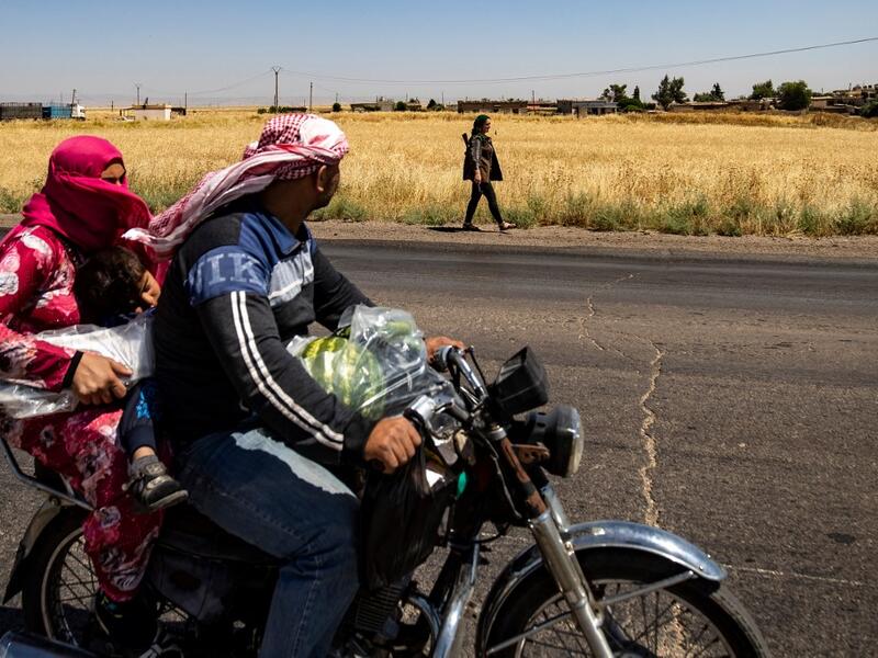 A family rider a motorcycle past a Kurdish female volunteer, from the newly formed Community Protection Forces, as she patrols a wheat field, against threats by jihadists to burn the crops, during harvest season on June 13, 2020, in the countryside east of Qamishli in Syria's northeastern Hasakah province. Delil SOULEIMAN / AFP
