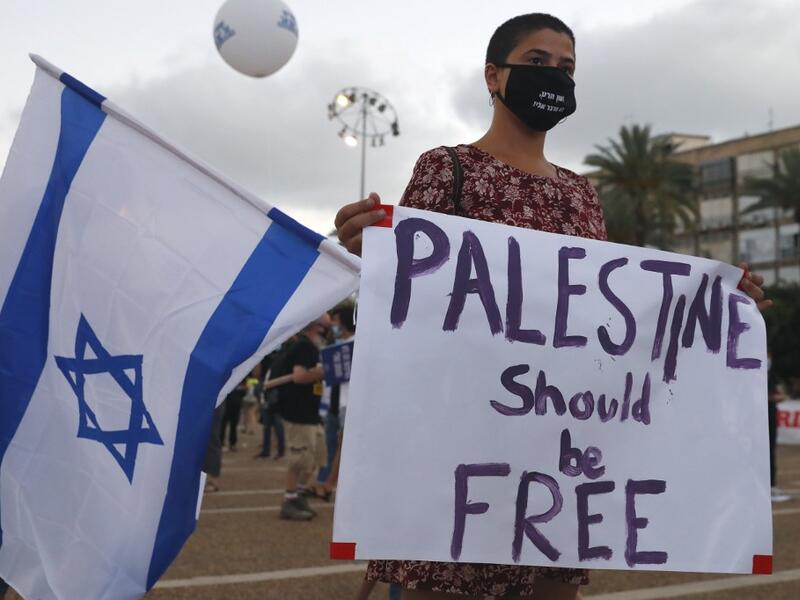 A protester, wearing a protective mask due to the COVID-19 pandemic, holds placards during a demonstration in Tel Aviv's Rabin Square to denounce Israel's plan to annex parts of the occupied West Bank, on June 23, 2020. Only a week before Prime Minister Benjamin Netanyahu intends to kick-start annexation plans in the occupied West Bank, Israel's premier is facing challenges at home and abroad. JACK GUEZ / AFP