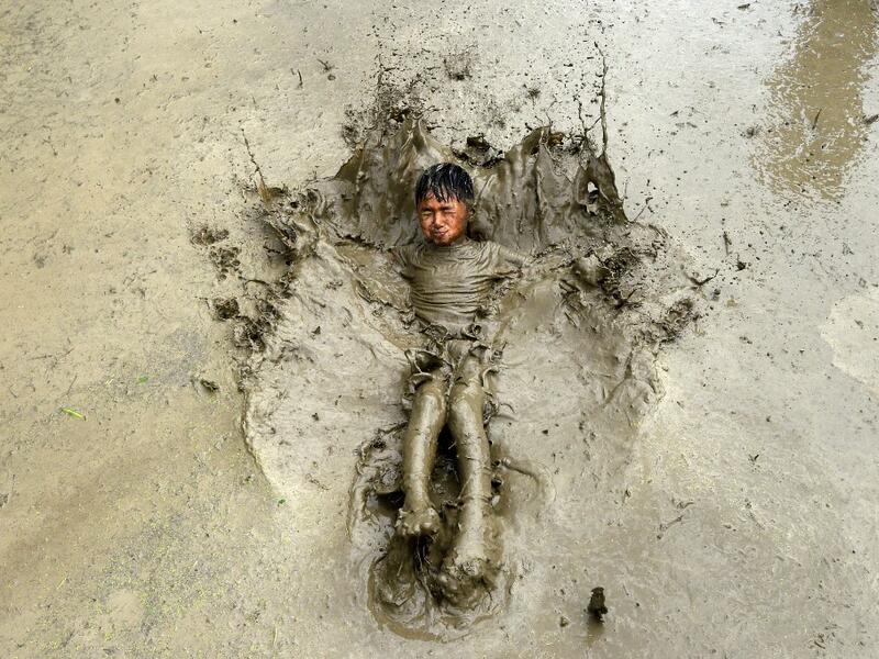 A boy plays in a rice paddy field during "National Paddy Day", which marks the start of the annual rice planting season, in Tokha village on the outskirts of Kathmandu on June 29, 2020. Splashing mud and drinking local rice beer, Nepali farmers this week celebrated National Paddy Day to mark the beginning of the rice-planting season, despite some coronavirus lockdown measures still in place. Traditional farming songs and laughter echoed in the air as farmers waded into waterlogged fields to sow green paddy.