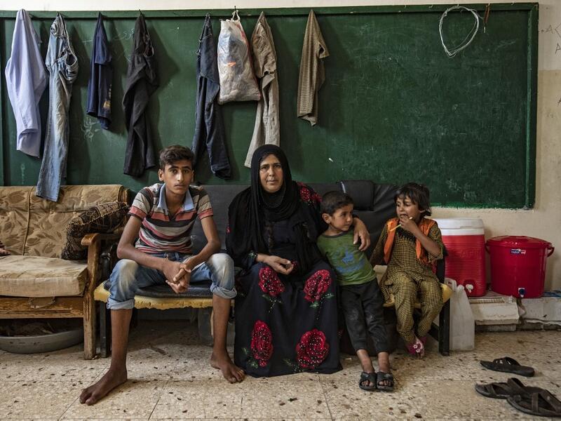A woman sits with children as they pose for a picture at a former classroom in a school building where Syrians -- displaced from the area of Ras al-Ain by the Turkish offensive on the northeast -- are staying in the city of Hasakah, on June 30, 2020. Delil SOULEIMAN / AFP