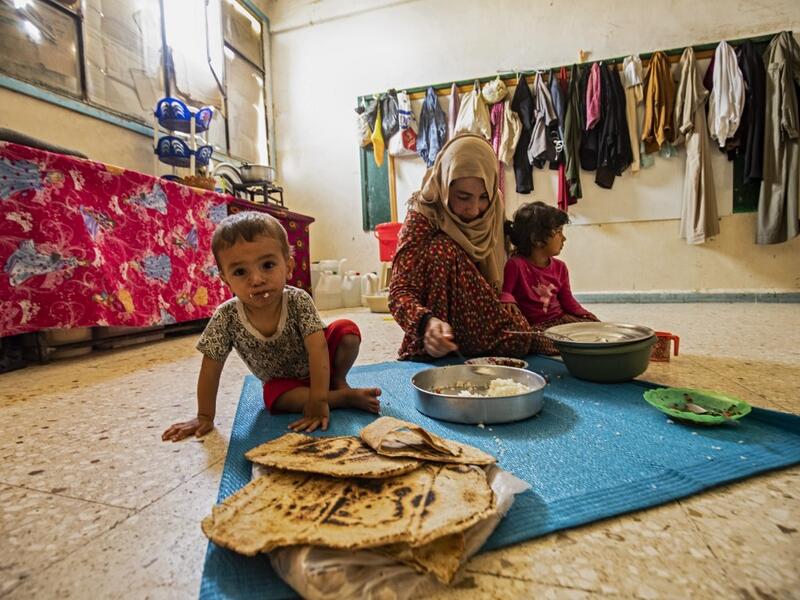 A woman feeds a child while sitting on the floor at a former classroom in a school building where Syrians -- displaced from the area of Ras al-Ain by the Turkish offensive on the northeast -- are staying in the city of Hasakah, on June 30, 2020. Delil SOULEIMAN / AFP