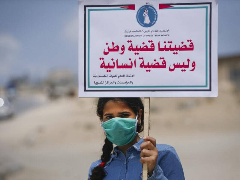 A Palestinian girl wearing a protective mask amid the COVID-19 pandemic lifts a placard which reads "Our cause that of a homeland, not a humanitarian one", during a rally for supporters of the Fateh movement against Israel's West Bank annexation plans, in Beit Hanun in the north of the Gaza Strip, on July 6, 2020. Mohammed ABED / AFP