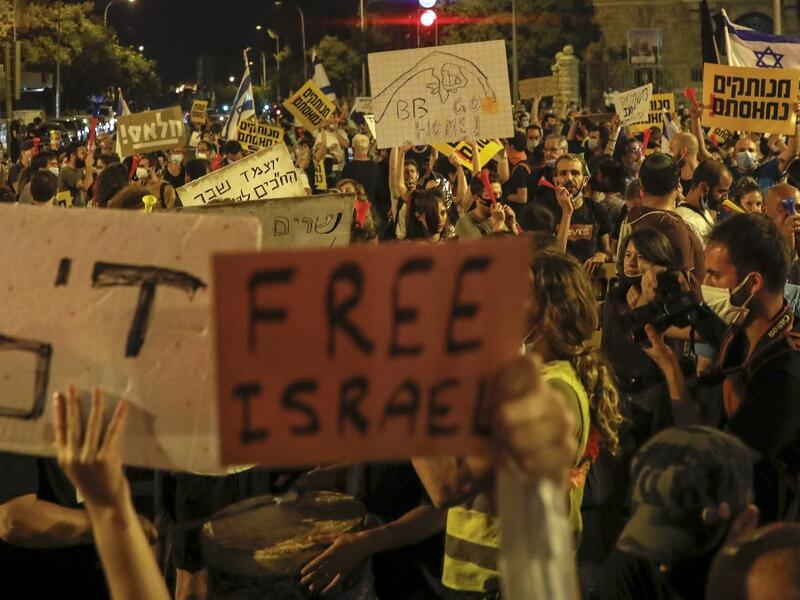 Israeli demonstrators lift placards during a rally against Prime Minister Benjamin Netanyahu outside his official residence in Jerusalem, on July 18, 2020, amid the coronavirus pandemic. Israeli police fired water cannons to disperse anti-government protests attended by thousands on Saturday, as public anger mounts over the handling of the coronavirus crisis. 