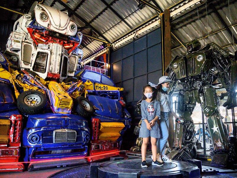 This photograph taken on July 18, 2020 shows children playing in front of a life-sized sculpture of a character from the "Transformers" film franchise made of scrap metal parts at the Ban Hun Lek museum in Ang Thong, some 100km north of Bangkok. "Ban Hun Lek" or "The House of Steel Robots" is a museum where a collective of artists display their scrap metal creations depicting popular comics and sci-fi film characters. Mladen ANTONOV / AFP