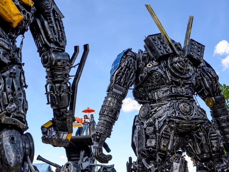This photograph taken on July 18, 2020 shows tourists taking photos of life-sized sculptures of characters from the "Transformers" film franchise made of scrap metal parts at the Ban Hun Lek museum in Ang Thong, some 100km north of Bangkok. "Ban Hun Lek" or "The House of Steel Robots" is a museum where a collective of artists display their scrap metal creations depicting popular comics and sci-fi film characters. Mladen ANTONOV / AFP