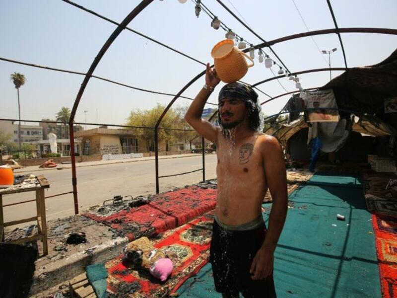 An Iraqi youth pours water over his head to cool down as temperatures soared in Baghdad, standing amid the remains of a protest tent that was burnt the previous night in the capital's Tahrir Square (AFP Photo/AHMAD AL-RUBAYE)