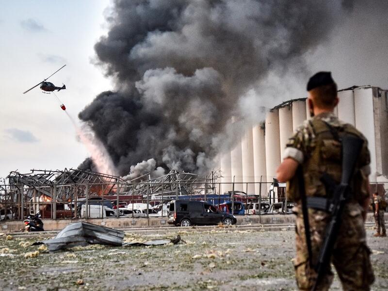 Lebanese army soldiers stand while behind a helicopter puts out a fire at the scene of an explosion at the port of Lebanon's capital Beirut on August 4, 2020. STR / AFP
