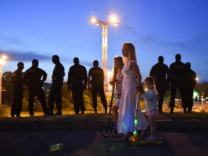 A woman with girls passes riot police officers guarding an area after polls closed in Belarus' presidential election, in Minsk on August 9, 2020. Sergei GAPON / AFP