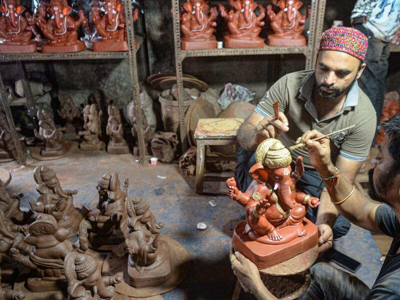In this picture taken on August 11, 2020, Muslim potter Yusuf Zakaria Galwani (L) instructs an artisan as he gives finishing touches to a clay idol of elephant headed Hindu god Ganesha at his workshop at Kumbharwada inside the Dharavi slums in Mumbai. After the coronavirus pandemic clobbered his pottery business, a Muslim artisan from India's largest slum turned to a Hindu god to revive his fortunes by making environmentally-friendly Ganesha idols for an upcoming festival. In Mumbai's Dharavi slum, Galwani 