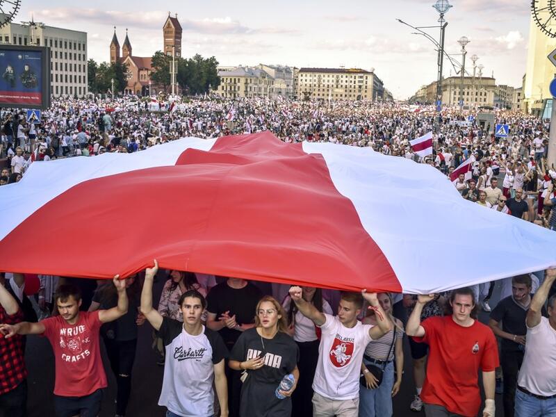 Belarus opposition supporters hold a giant former white-red-white flag of Belarus used in opposition to the government, during a demonstration in central Minsk on August 16, 2020. The Belarusian strongman, who has ruled his ex-Soviet country with an iron grip since 1994, is under increasing pressure from the streets and abroad over his claim to have won re-election on August 9, with 80 percent of the vote. Sergei GAPON / AFP