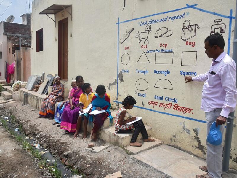 In this picture taken on August 27, 2020, Kalidas Chavdekar, a school teacher of Aasha Marathi Vidyalay points to a writing from textbooks of various subjects painted on the wall of a house to teach students who are unable to carry smartphones to attend online school classes amid Covid-19 coronavirus pandemic in Solapur, in Maharashtra state. AFP