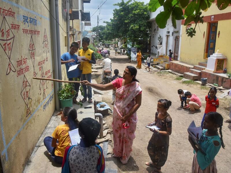 Half a dozen children in an Indian village gather around their teacher as she points a stick at a lesson painted on a wall, one of many which are part of an unusual effort to help poor students keep up with their education amid the coronavirus pandemic. AFP