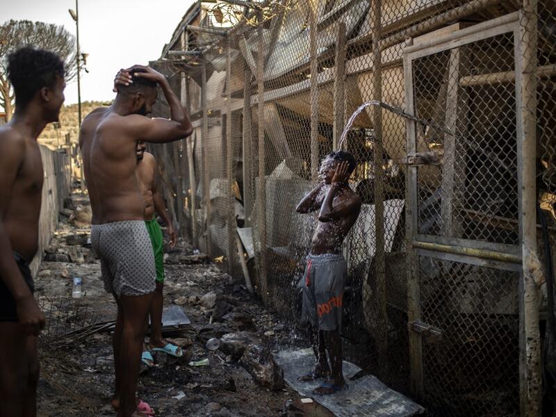 Migrants take shower Children walk in the burnt migrants camp of Moria on the Greek Aegean island of Lesbos on September 9, 2020 after a major fire broke out. Thousands of asylum seekers were left homeless on September 9 after a fire gutted Greece's largest migrant camp on Lesbos, plunging the island into crisis and provoking an outpouring of sympathy from around Europe and calls for reform of the refugee system. 
