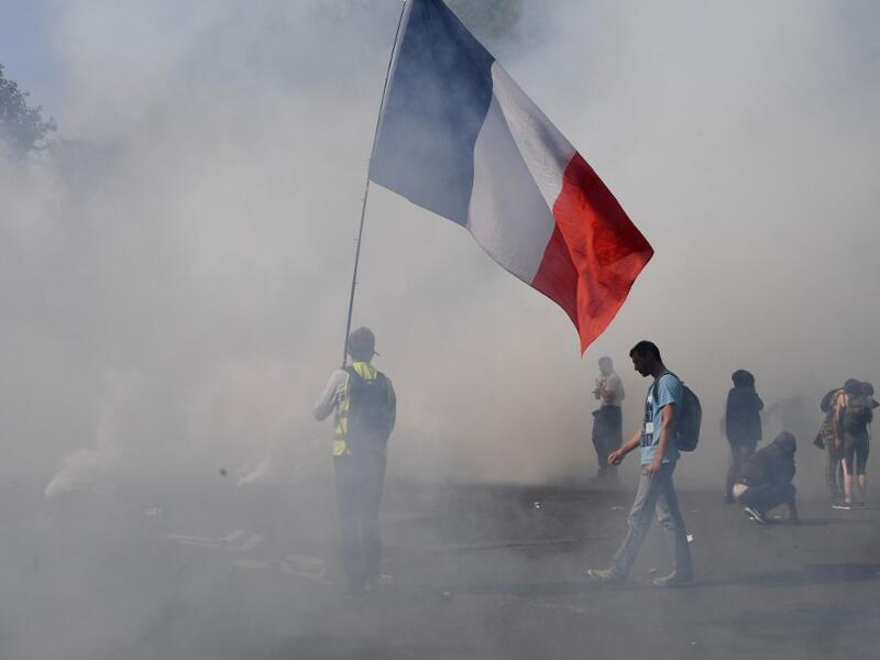 A protester holds a French national flag surrounded by smoke of tear gas during a demonstration called by the "yellow vest" (gilets jaunes) movement on September 12, 2020 in Paris. Alain JOCARD / AFP