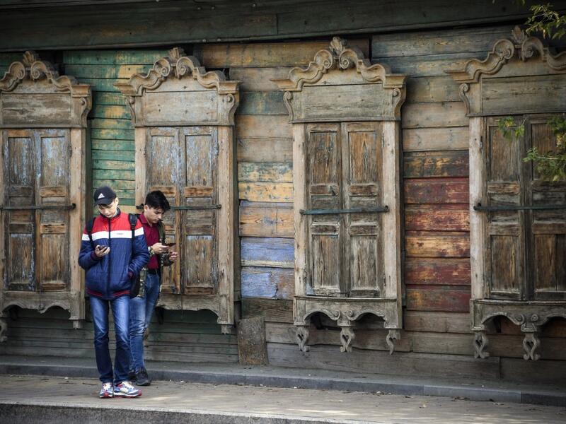 People stand in front of a traditional wooden house in the Siberian city of Tomsk on September 8, 2020. Tomsk is considered to be one of the oldest towns in Siberia founded in 1604. Wooden architecture is one of the symbols of the city of Tomsk, its distinctive feature. Today Tomsk is the only city in Siberia where the background wooden buildings have been preserved, reflecting the manor structure of the city streets. Unfortunately, many wooden houses are not in very good condition and require restoration. 