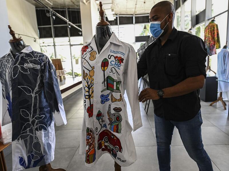 A gallery worker organizes white coats used by doctors fighting against COVID-19 and decorated by Panamanian artists, in Panama City, on September 26, 2020. More than 20 doctor's coats fighting against COVID-19 that were disinfected and painted by Panamanian artists will be auctioned off from October 1 to 4. The funds will go to 20 health centers. Luis ACOSTA / AFP