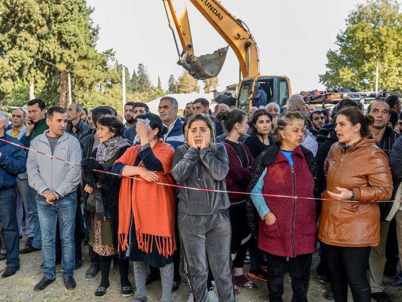 People stand behind caution tape as rescuers search for victims or survivors at the blast site hit by a rocket during the fighting between Armenia and Azerbaijan over the breakaway region of Nagorno-Karabakh, in the city of Ganja, Azerbaijan, on October 11, 2020. Bulent Kilic / AFP