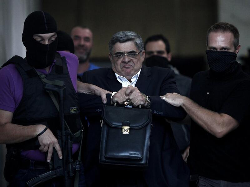  In this file photo taken on September 28, 2013 the leader of ultra-right wing Golden Dawn party Nikos Michaloliakos is escorted by masked police officers to the prosecutor from the police headquarters in Athens. A Greek court on October 14, 2020 handed a 13-year prison sentence to the leader of neo-Nazi group Golden Dawn for running a criminal organisation. As well as Nikos Michaloliakos, the party's founder -- who received an additional one year for illegal possession of a weapon -- the court also sentenc
