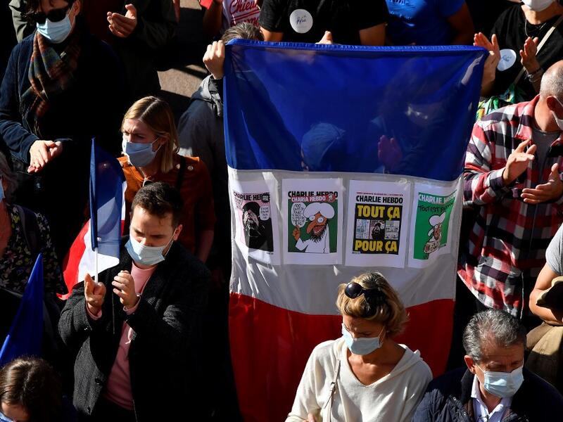 A person holds a French national flag with front covers of Charlie Hebdo satirical magazine as people gather on Place du Capitole in Toulouse on October 18, 2020, in homage to history teacher Samuel Paty two days after he was beheaded by an attacker who was shot dead by policemen. GEORGES GOBET / AFP