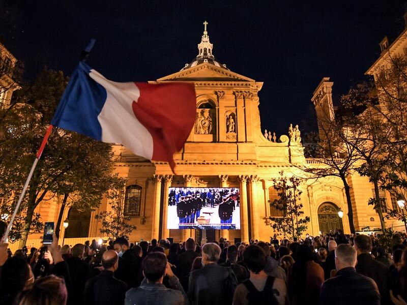 An attendee waves a French flag as people gather on the Place de la Sorbonne in Paris on October 21, 2020, to watch a live broadcast on a giant screen of a national homage at the Sorbonne University to French teacher Samuel Paty, who was beheaded for showing cartoons of the Prophet Mohamed in his civics class. Bertrand GUAY / AFP