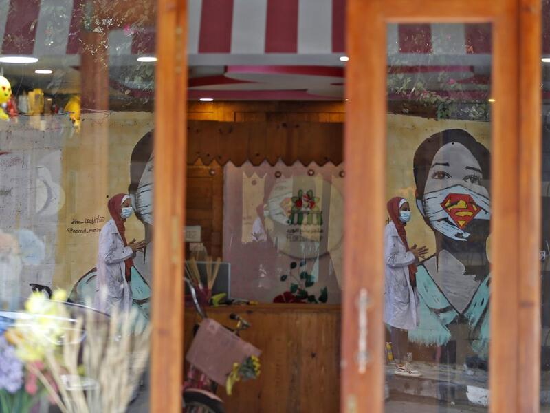The image of a Palestinian student painting a large mural of a mask-clad girl is reflected on the doors of a shop in Gaza City on October 22, 2020, amid the novel coronavirus pandemic crises. Mohammed ABED / AFP