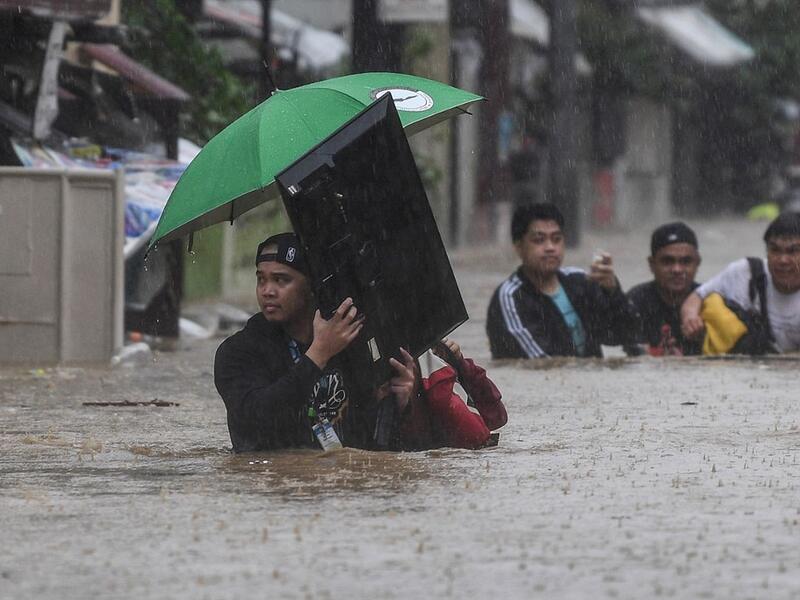 A man (L) carries a television as residents make their way through a flooded street to shelter after Typhoon Vamco hit the area in Marikina City, suburban Manila on November 12, 2020. Ted ALJIBE / AFP